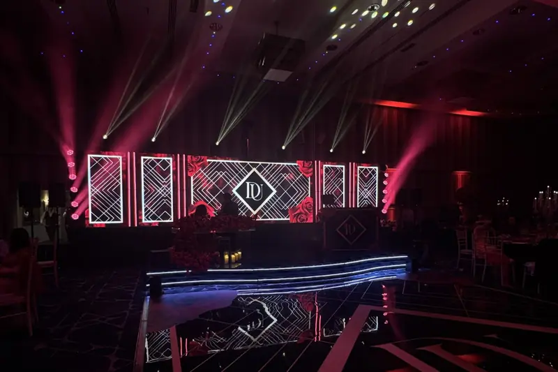 The finished stage on the night: lit LED panels with the monogram, red and white beams, curved LED riser